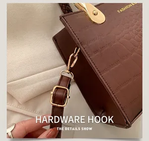 Detail of gold hardware hook and adjustable strap on brown crocodile texture handbag