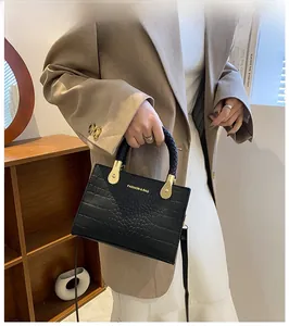 Detail of black crocodile texture handbag with gold hardware and woven handle