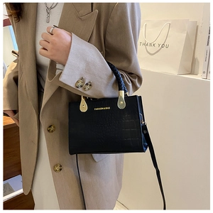 Detail of black faux-crocodile leather handbag with gold horsebit buckle and woven handle