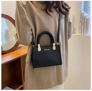 Detail of black faux leather bag with crocodile texture and woven handles on a model