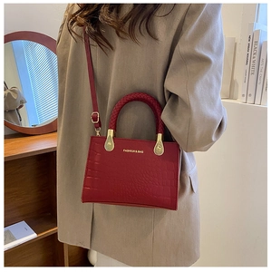 Detail of red croc-embossed handbag with gold lettering and woven handle on a model