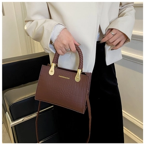 Detailed shot of brown crocodile pattern handbag with woven handles and golden hardware