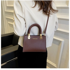 Detailed side view of a brown crocodile pattern handbag with woven handle and gold logo