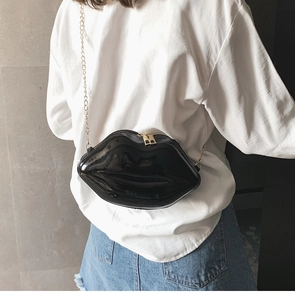 Detail of a chic black glossy lip-shaped crossbody bag with a gold chain strap
