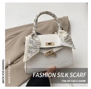 Close-up of white croc-embossed handbag with silk scarf and gold lock detail