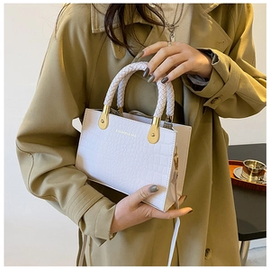 Detail of white crocodile pattern handbag with woven handle and gold metal accents