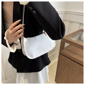 Primer plano de un bolso baguette de charol blanco combinado con una chaqueta negra
