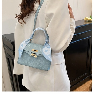 Detail of light blue crocodile-embossed handbag with gold clasp and silk scarf