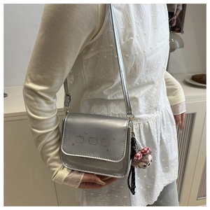Close-up of silver metallic crossbody bag with pink cartoon bear and plush charm