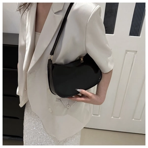 Detalle del bolso de charol negro brillante con cremallera dorada y correa fina