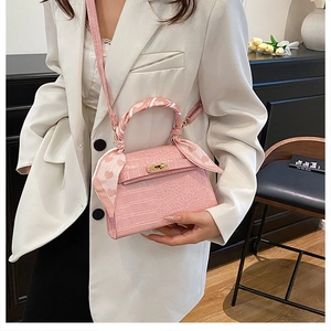 Detail of pink croc-patterned handbag with golden turn-lock and heart-print silk scarf