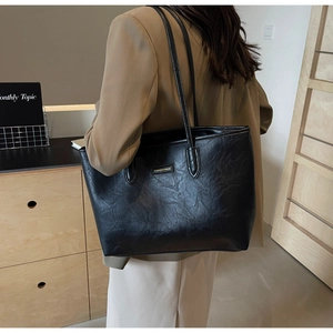 Detail of large black tote bag featuring crinkled leather texture and gold logo