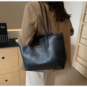 Detail of black tote bag with wrinkled leather texture and golden FASHION logo