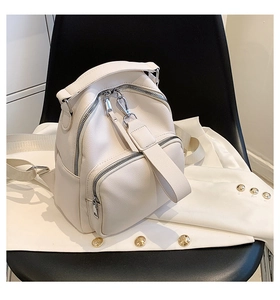 Close-up of white mini backpack with lychee texture and silver zippers on a black chair