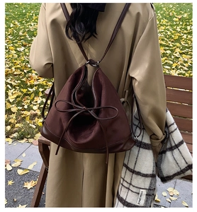 Detail of dark brown backpack with slender bow tie and metallic hardware on shoulder straps