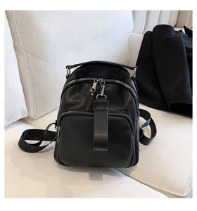 Close-up of black litchi pattern leather backpack with silver zippers on a soft fabric sofa