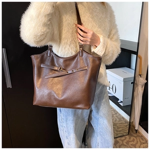 Detail view of a vintage brown leather tote bag featuring gold hardware and strap accents