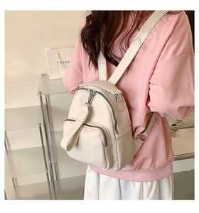 Rear view of model wearing a creamy white faux leather backpack with adjustable straps
