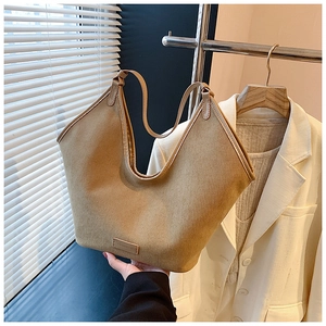 Detail view of a large brown canvas tote bag with slim straps and rectangular leather logo patch
