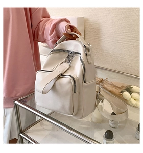 Detail of a white PU leather backpack featuring silver hardware and wide fabric straps