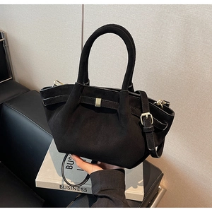 Detail einer schwarzen Wildleder-Handtasche mit goldener Metallschnalle und Schultergurt