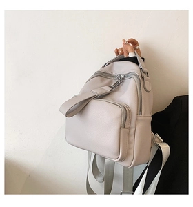 Detail of light grey PU leather backpack featuring silver zippers and pebbled texture