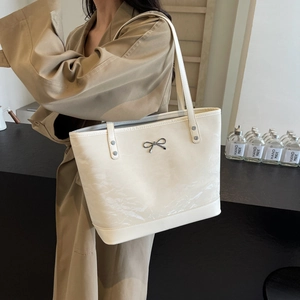 Grand sac cabas crème avec texture plissée et nœud argenté porté par un mannequin