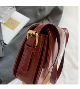 Detail of burgundy glossy leather bag with vintage gold adjustment buckle on the side