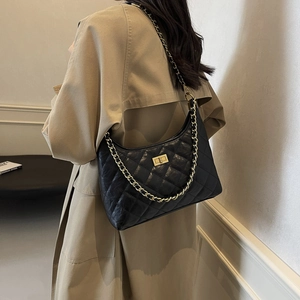 Quilted black leather tote bag with gold chain strap shown on a model in a trench coat