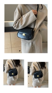 Detail view of black faux leather crossbody bag with golden buckle on neutral background