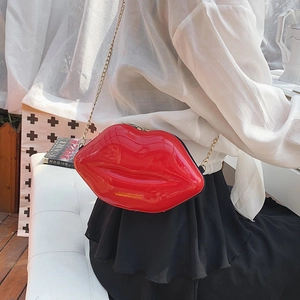 Chic red lip-shaped crossbody bag with gold chain strap worn by a model in soft lighting
