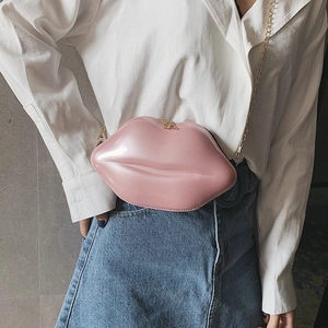 Pink lip-shaped crossbody bag with gold chain strap worn by a model in a casual outfit
