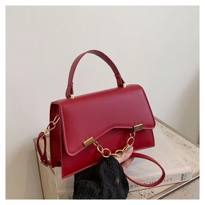 Detail of dark red square bag featuring gold chain trim and metallic buckle closure