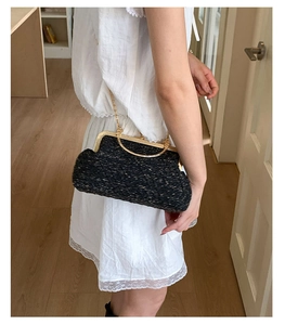 Détail du sac coquille tissé noir avec poignées rondes dorées et bandoulière chaîne