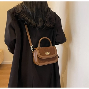 Detailed view of vintage brown crossbody bag with suede stitching and metal lock on model