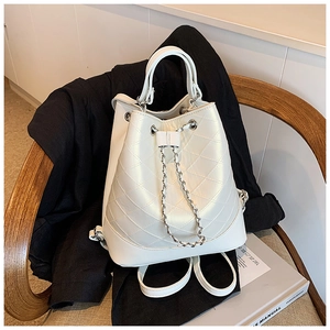 Detail view of pearl white quilted bucket bag with chain drawstring on a wooden chair