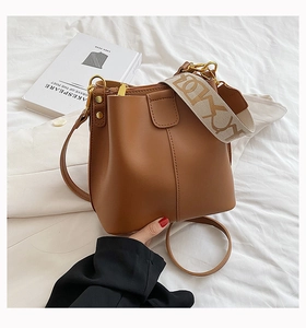 Détail d'un sac seau en cuir marron avec large bandoulière tissée et boucle dorée