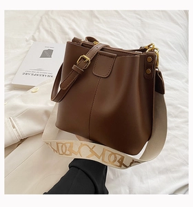 Détail du sac seau en cuir marron foncé avec bandoulière brodée et boucles dorées