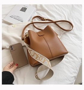 Détail du sac seau en cuir marron avec large bandoulière jacquard et boucles dorées