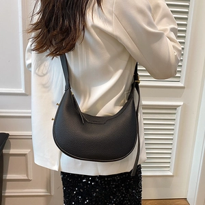 Minimalist black pebble leather half-moon shoulder bag with golden hardware on a model