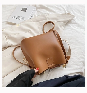 Détail du sac seau en cuir marron avec large bandoulière en tissu réglable sur tissu blanc