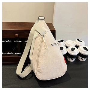 Détail du sac de poitrine en toile beige avec logo en métal et bandoulière réglable