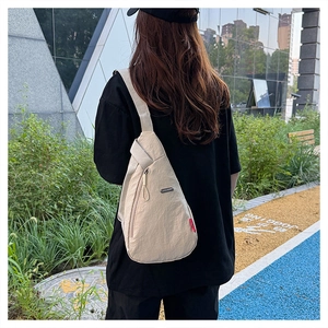 Gros plan d'un sac de poitrine en nylon beige clair avec sangle réglable et détail rouge
