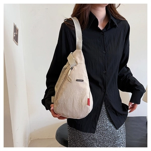 Détail du sac de poitrine minimaliste beige en nylon avec logo noir et étiquette rouge