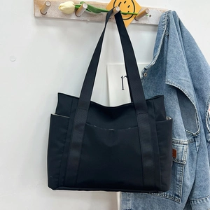 Close-up of black canvas tote bag hanging on wooden hook in a casual lifestyle setting