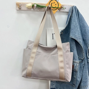 Detail of gray nylon tote bag with wide straps and side pocket hanging on a wooden hook