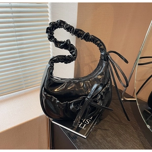 Detail of black glossy pleated shoulder bag featuring a large bow and cloud handle
