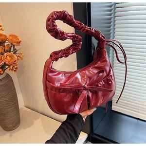 Detail of red glossy pleated underarm bag with bow decoration and cloud-style handle