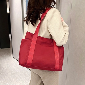 Rear view of a red nylon tote bag with wide strap on a model in beige suit for daily use