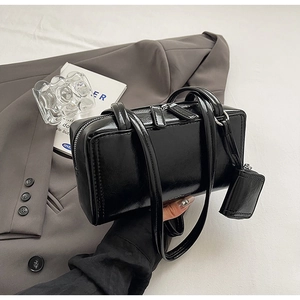 Detail of glossy black leather bowling bag featuring dual zippers and mini charm pouch